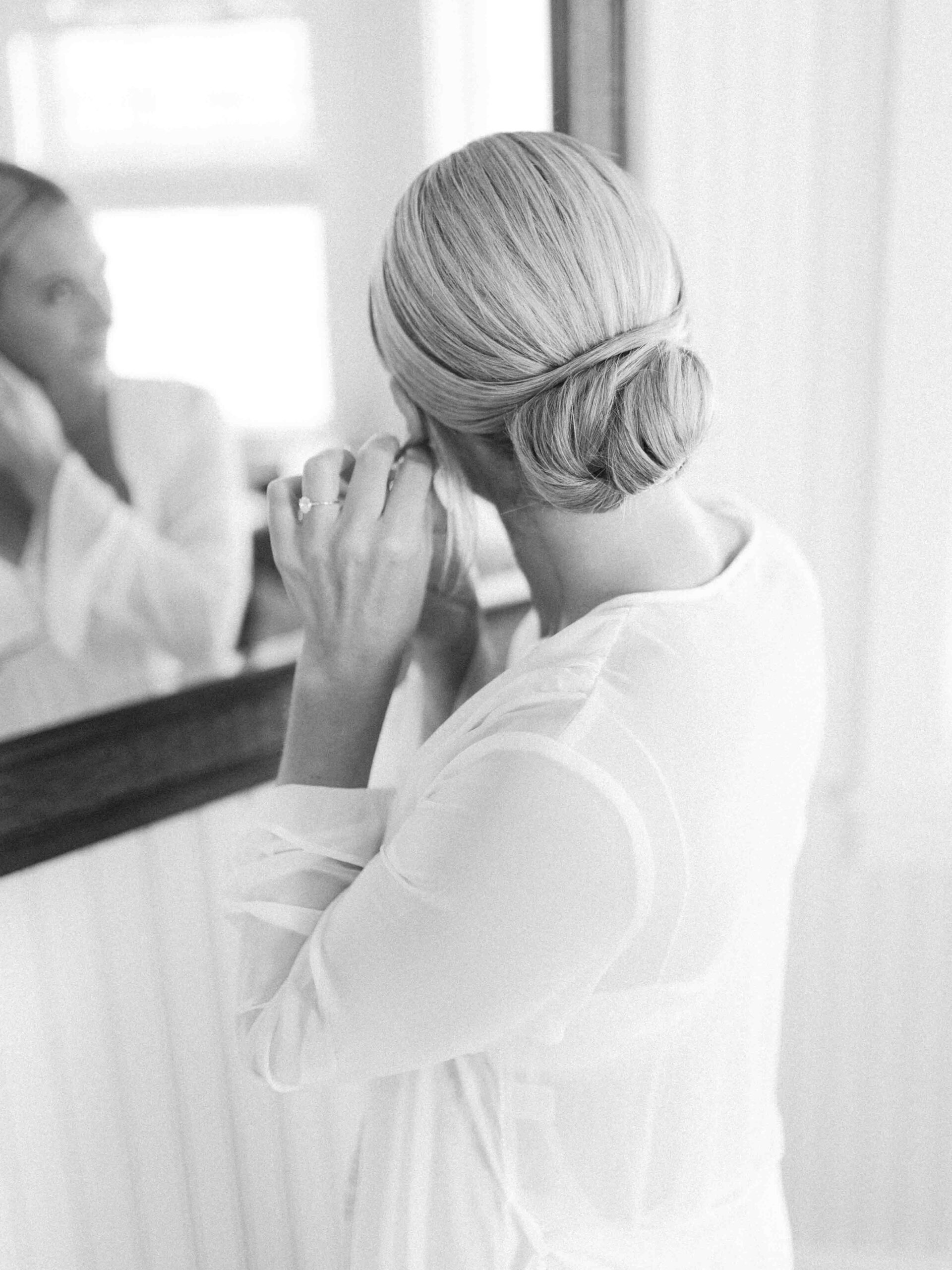 Bride looking in the mirror, putting her earring in 