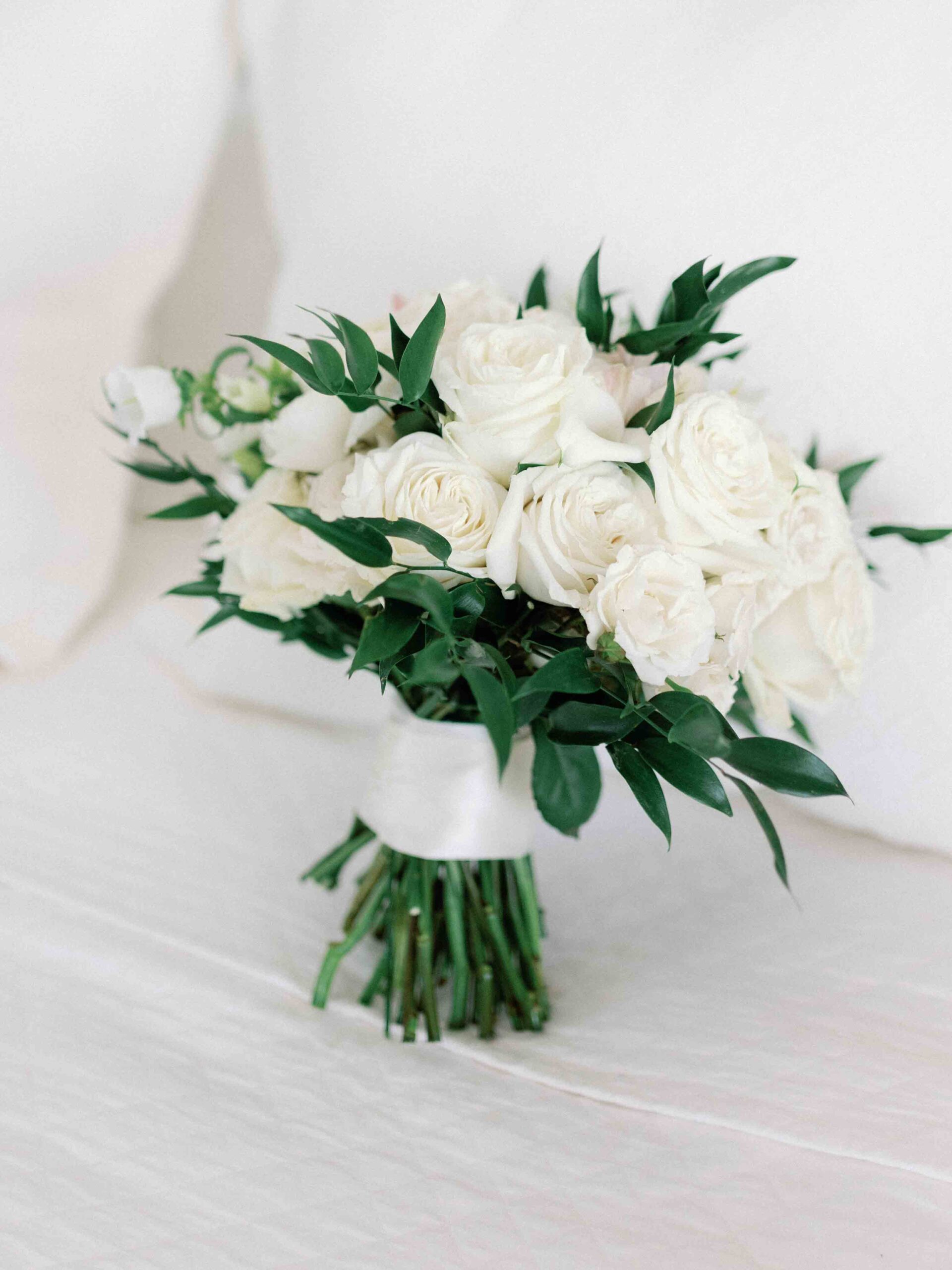 White rose wedding bouqet by Florals by Kait on a bed