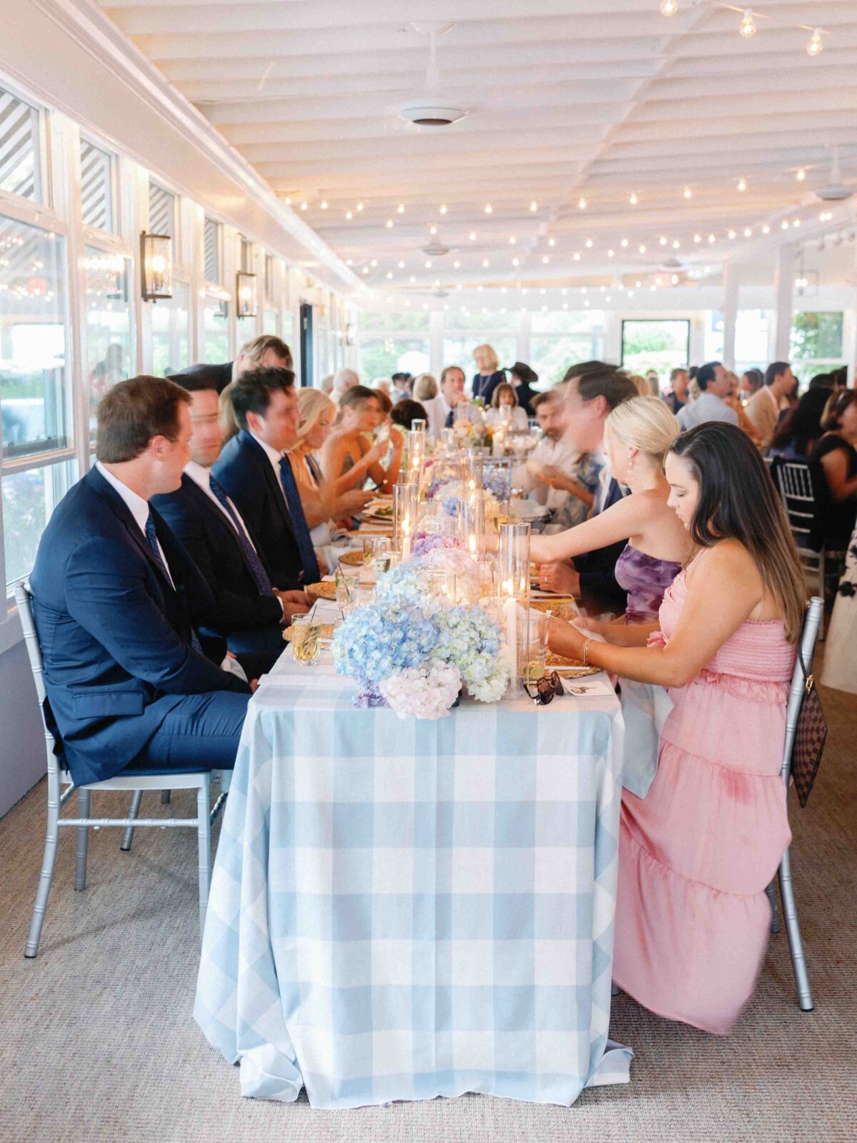Wedding party sitting down for candle lit dinner with checkered blue and white table cloth 
