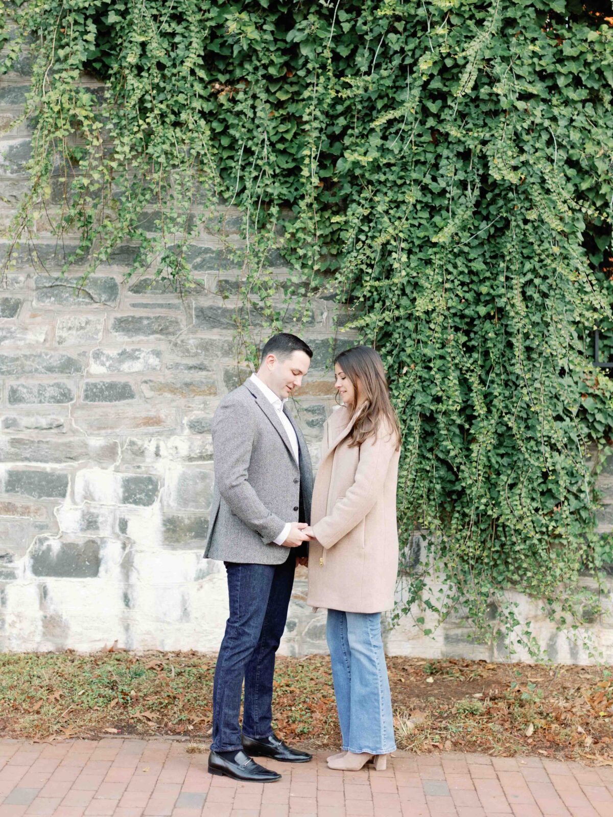 Couple holding hands. Green vines on a stone wall are above them